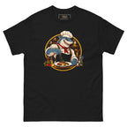 Kitchen Shark tee, black, front: illustration of a grinning shark chef in a toque and red neckerchief seasoning a plate of grilled salmon, framed by a gold circle with copper pans behind