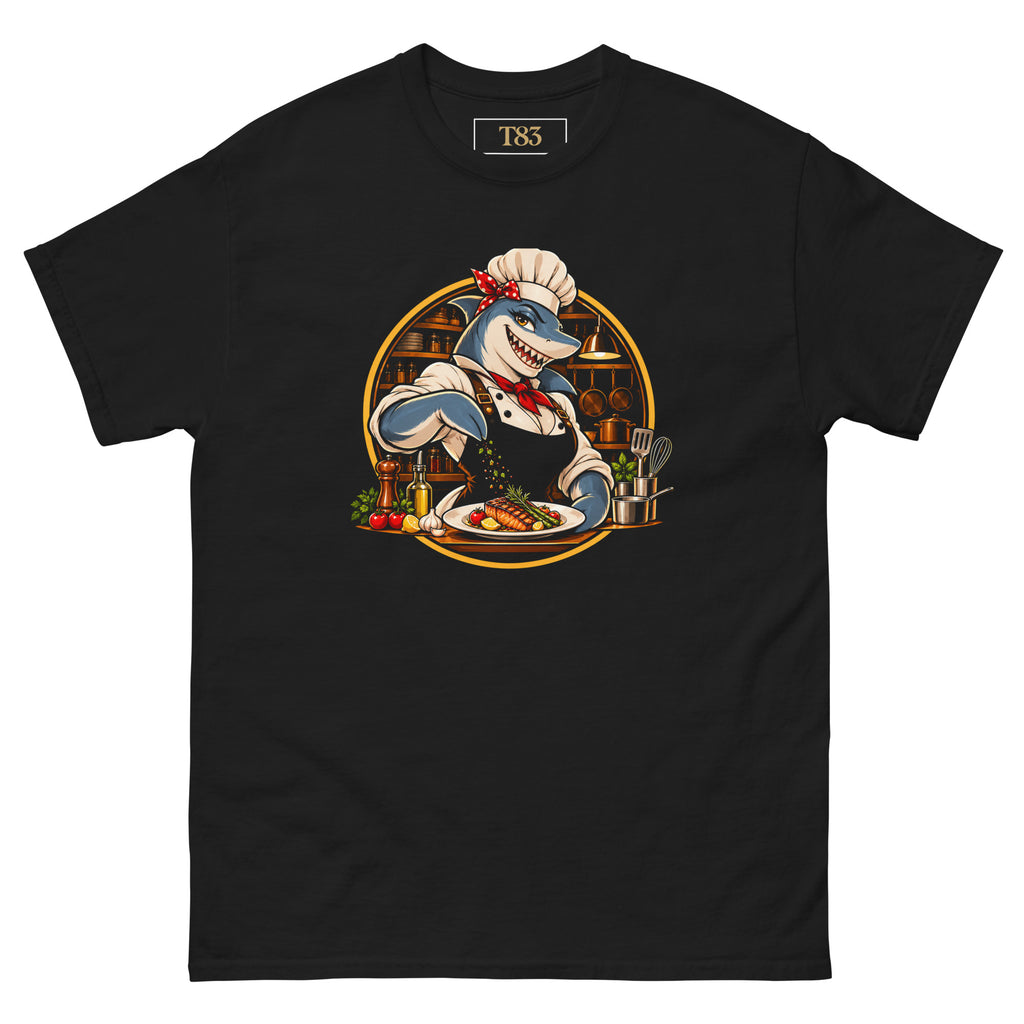 Kitchen Shark (Her) tee, black, front: illustration of a grinning shark chef in a toque, red polka-dot bandana and red neckerchief seasoning a plate of grilled salmon, framed by a gold circle with copper pans behind